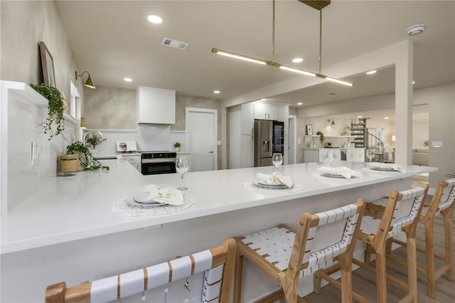 kitchen featuring stainless steel appliances, a peninsula, white cabinetry, light countertops, and wood finished floors