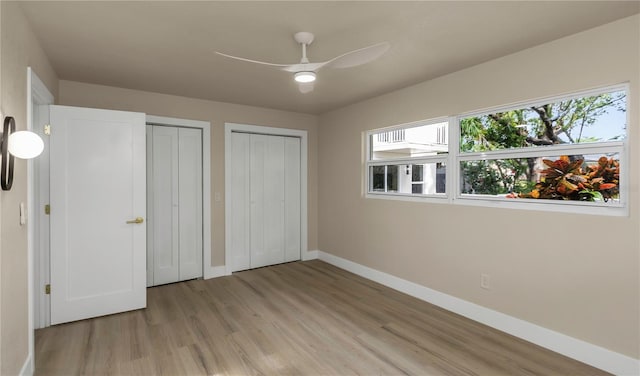 unfurnished bedroom with two closets, baseboards, light wood-style flooring, and multiple windows