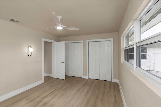 unfurnished bedroom featuring two closets, light wood finished floors, and baseboards