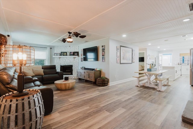 living room featuring ceiling fan, a stone fireplace, recessed lighting, baseboards, and light wood-type flooring