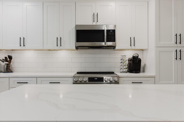kitchen featuring stove, stainless steel microwave, backsplash, and white cabinetry