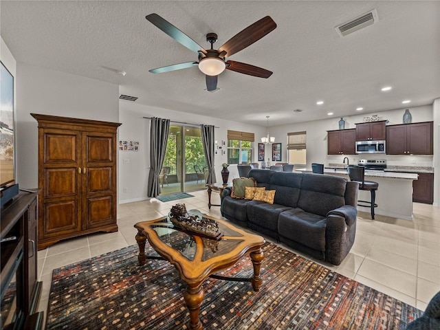 living room featuring visible vents, light tile patterned flooring, and ceiling fan with notable chandelier