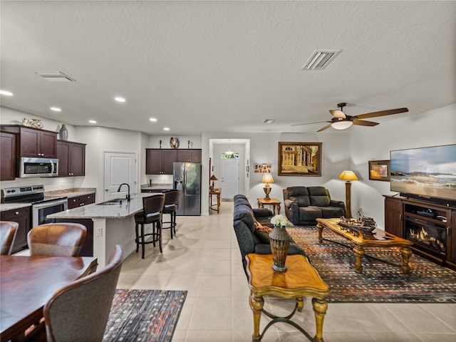 living area with light tile patterned floors, a textured ceiling, visible vents, and a ceiling fan