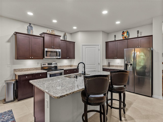 kitchen featuring a sink, stainless steel appliances, a kitchen breakfast bar, a center island with sink, and light stone counters