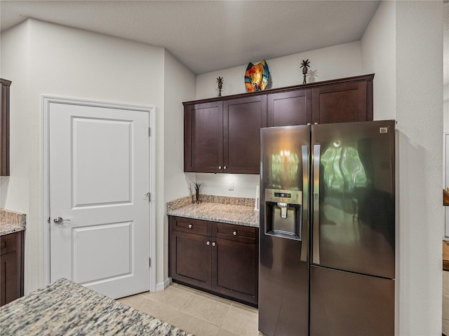 kitchen with dark brown cabinetry, light tile patterned flooring, stainless steel fridge with ice dispenser, and light stone counters