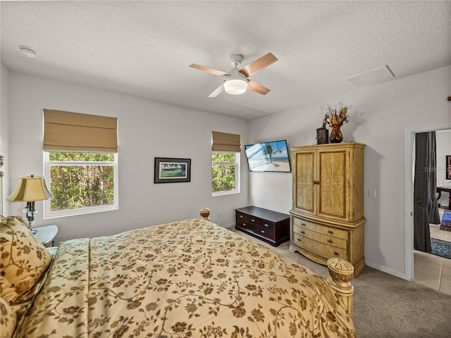 bedroom featuring light colored carpet, a textured ceiling, visible vents, ceiling fan, and baseboards