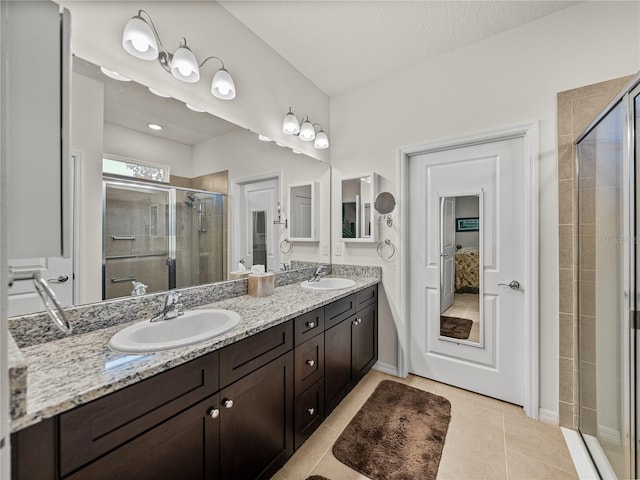 ensuite bathroom with a sink, double vanity, a shower stall, and tile patterned floors