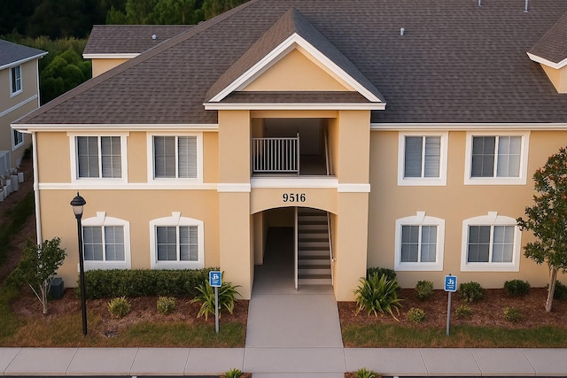 townhome / multi-family property with a shingled roof, stucco siding, and a balcony