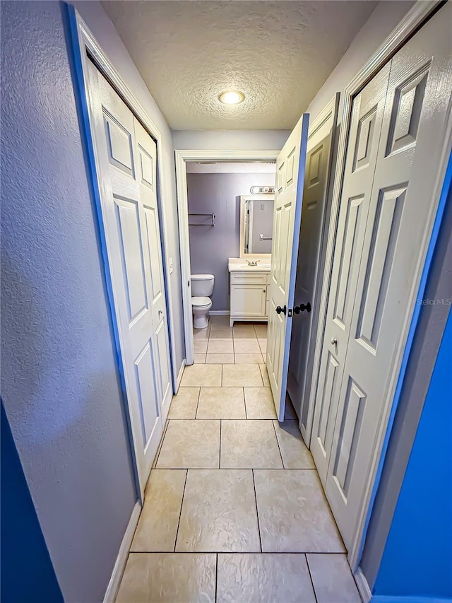 hall with baseboards, a textured ceiling, and light tile patterned floors