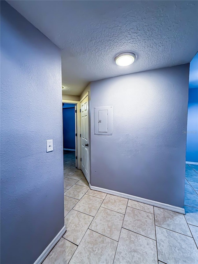 hallway featuring a textured ceiling, baseboards, a textured wall, and light tile patterned floors