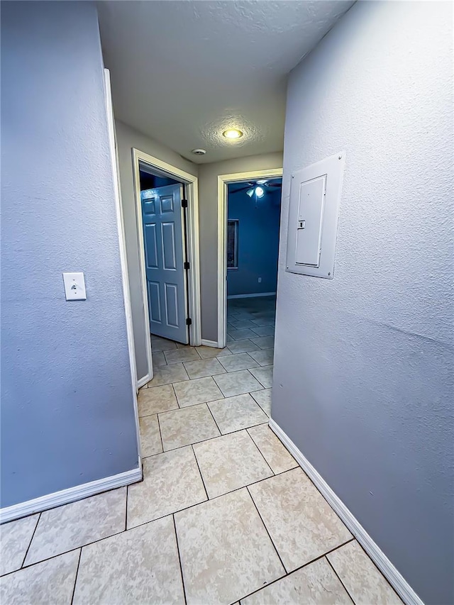 corridor with baseboards, a textured wall, electric panel, and light tile patterned flooring