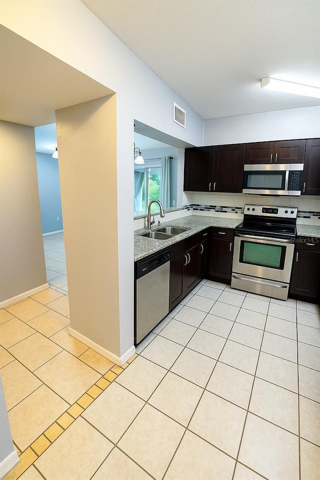 kitchen with light tile patterned flooring, light stone countertops, a sink, stainless steel appliances, and visible vents