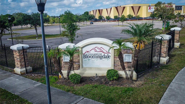 community sign featuring uncovered parking and fence