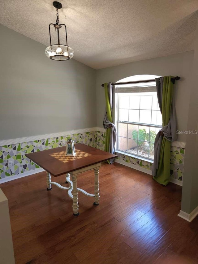 dining area with wainscoting, wallpapered walls, a textured ceiling, and wood finished floors