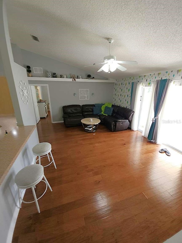 living room featuring a ceiling fan, a textured ceiling, visible vents, wood finished floors, and lofted ceiling