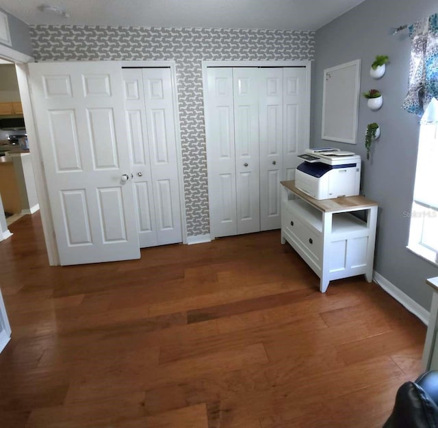 unfurnished bedroom featuring baseboards, two closets, and wood finished floors
