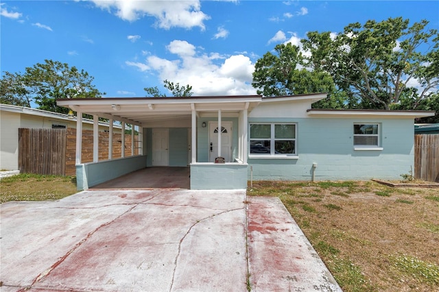 ranch-style home featuring a carport, concrete block siding, fence, and concrete driveway