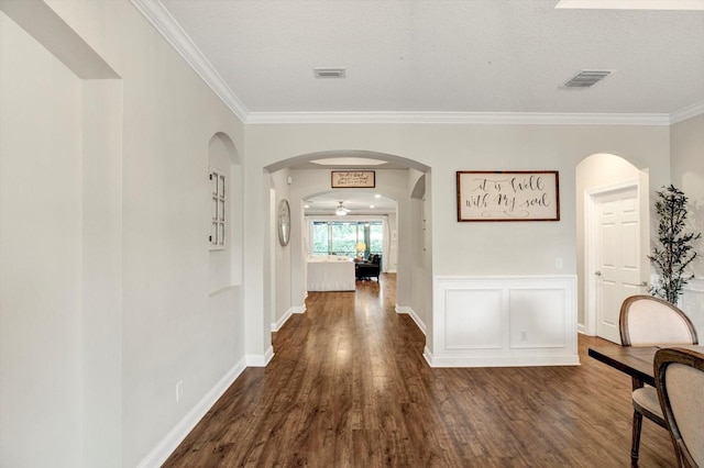 hallway with crown molding, arched walkways, dark wood-style flooring, and visible vents