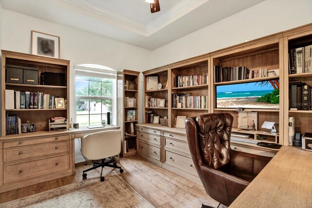 office space with crown molding, a tray ceiling, built in desk, and light wood-type flooring
