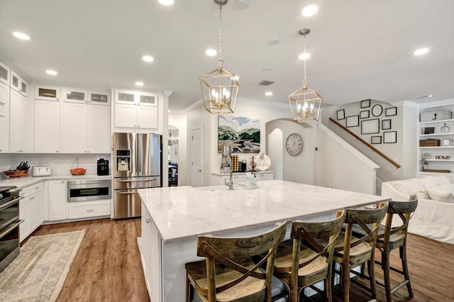 kitchen featuring ornamental molding, a center island with sink, stainless steel fridge with ice dispenser, light stone counters, and arched walkways