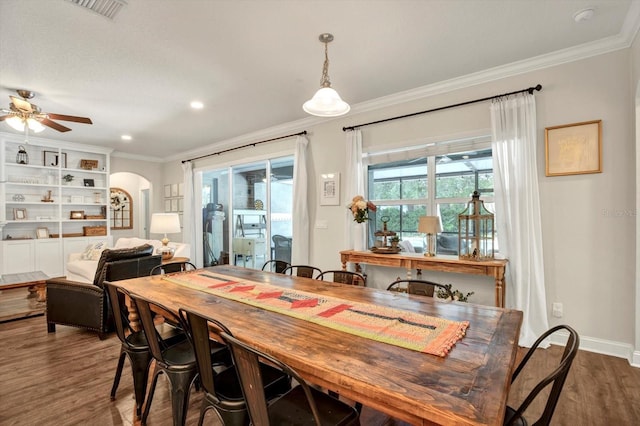 dining space with arched walkways, a ceiling fan, wood finished floors, visible vents, and ornamental molding