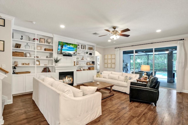 living area featuring crown molding, ceiling fan, a glass covered fireplace, dark wood finished floors, and visible vents