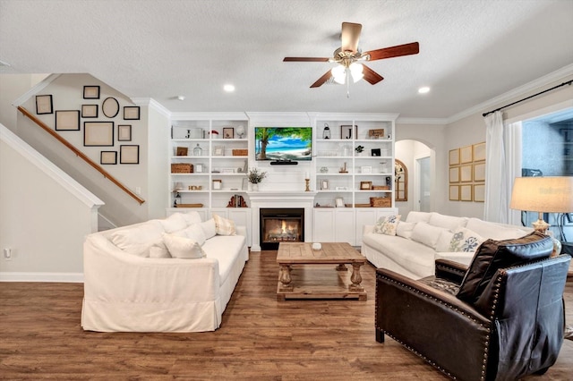 living area with crown molding, arched walkways, a textured ceiling, a ceiling fan, and wood finished floors