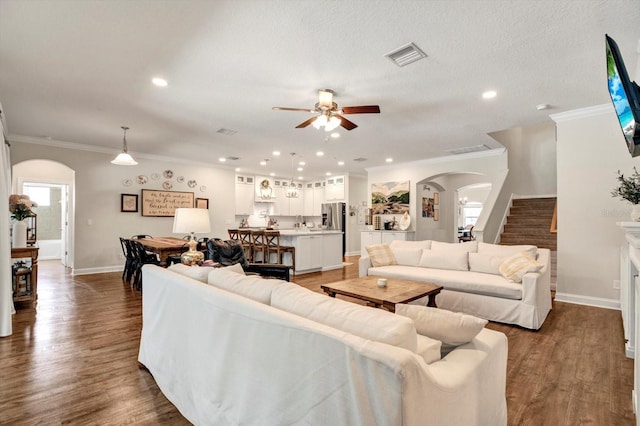 living room with crown molding, arched walkways, stairway, and a ceiling fan
