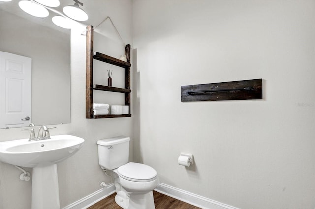 half bath featuring toilet, baseboards, a sink, and wood finished floors