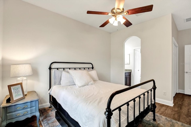 bedroom featuring arched walkways, baseboards, wood finished floors, ensuite bathroom, and visible vents