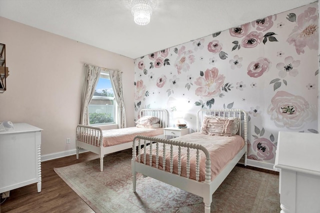 bedroom with baseboards, an accent wall, wallpapered walls, and wood finished floors
