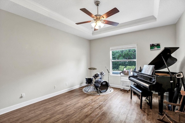 living area featuring ornamental molding, wood finished floors, baseboards, ceiling fan, and a raised ceiling