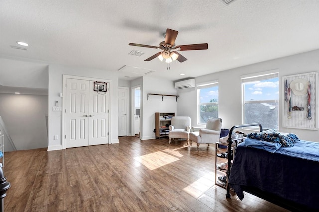 bedroom with a textured ceiling, a wall mounted AC, wood finished floors, and visible vents