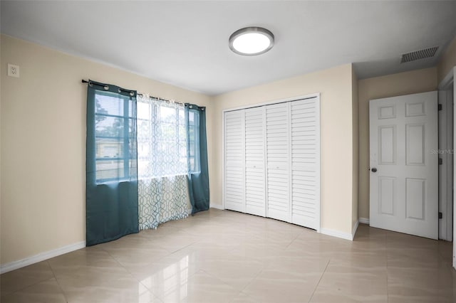unfurnished bedroom with baseboards, visible vents, light tile patterned floors, and a closet