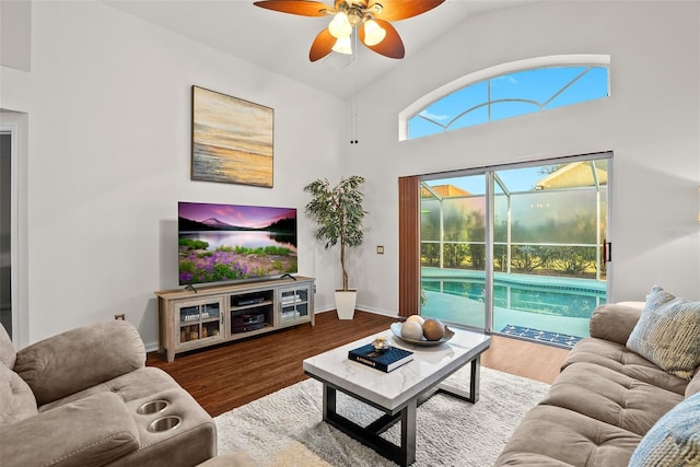 living area featuring wood finished floors, baseboards, ceiling fan, a sunroom, and high vaulted ceiling