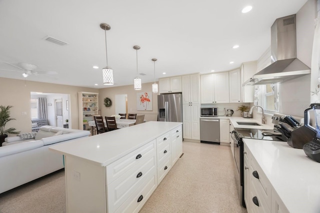 kitchen featuring appliances with stainless steel finishes, a sink, wall chimney exhaust hood, a kitchen island, and visible vents