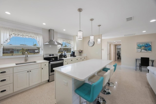 kitchen with wall chimney range hood, stainless steel range with electric cooktop, a sink, a center island, and a kitchen bar