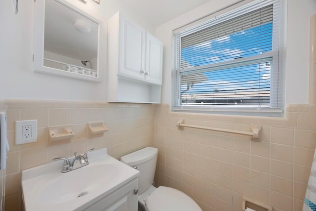 bathroom with toilet, tile walls, wainscoting, and vanity
