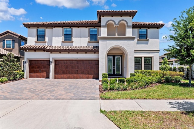 mediterranean / spanish-style house with a tiled roof, decorative driveway, fence, an attached garage, and stucco siding