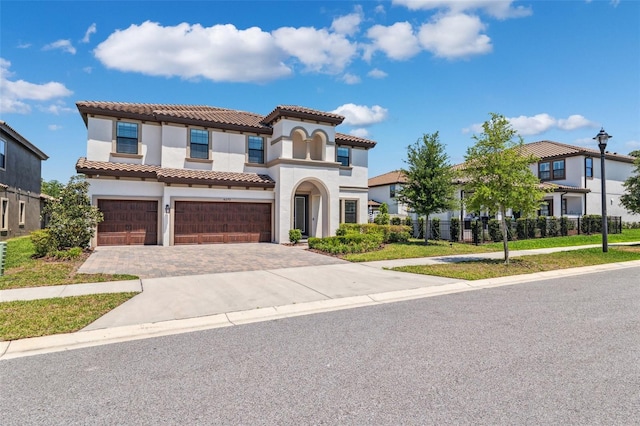 mediterranean / spanish home featuring stucco siding, an attached garage, a tile roof, and decorative driveway