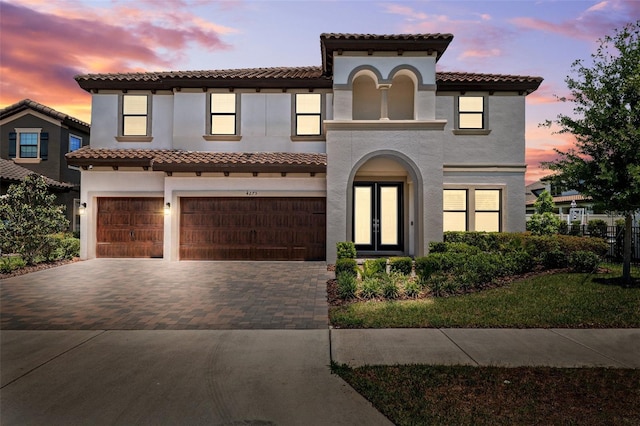 mediterranean / spanish home featuring stucco siding, french doors, a tiled roof, an attached garage, and driveway