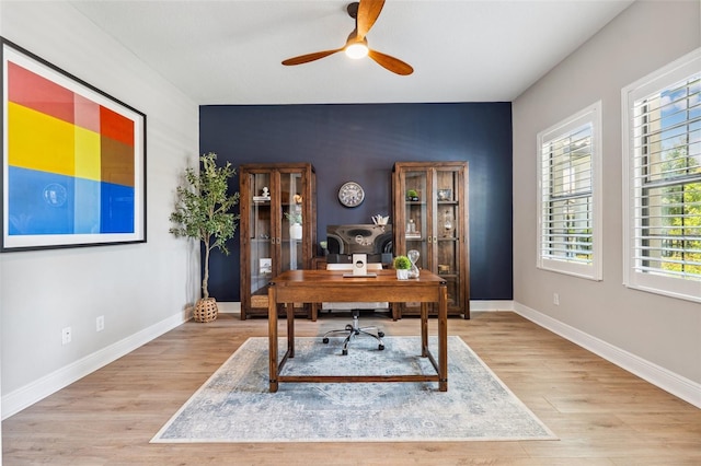 home office with baseboards, an accent wall, ceiling fan, and wood finished floors