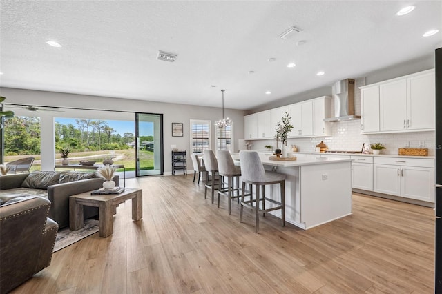 kitchen with visible vents, open floor plan, wall chimney range hood, recessed lighting, and light countertops