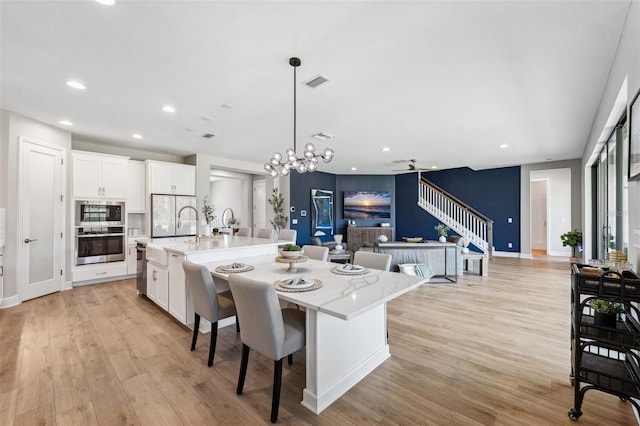 kitchen featuring appliances with stainless steel finishes, an island with sink, light wood-style flooring, white cabinetry, and visible vents