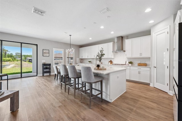 kitchen with wall chimney range hood, decorative backsplash, visible vents, a center island, and light countertops