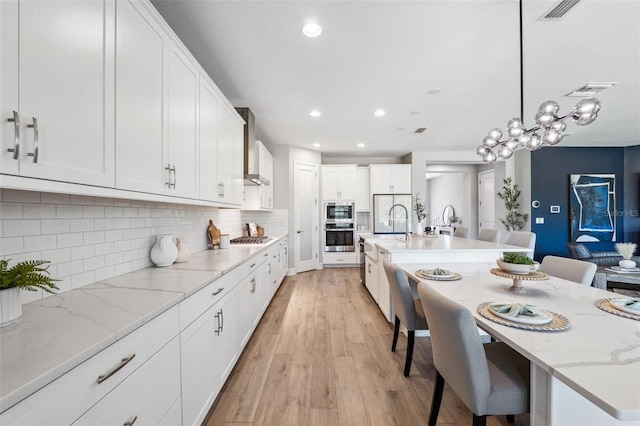 kitchen with visible vents, a large island with sink, white cabinets, light wood finished floors, and stainless steel appliances