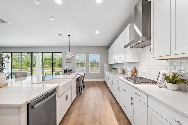 kitchen with baseboards, wall chimney exhaust hood, a sink, light wood-style flooring, and stainless steel appliances