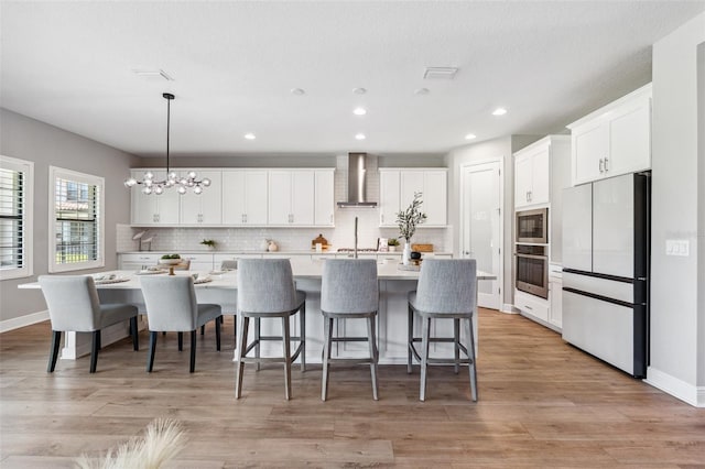 kitchen featuring wall chimney range hood, backsplash, appliances with stainless steel finishes, light countertops, and white cabinets