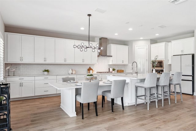 kitchen featuring light countertops, a breakfast bar area, wall chimney exhaust hood, freestanding refrigerator, and tasteful backsplash