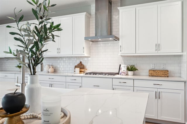 kitchen featuring decorative backsplash, wall chimney exhaust hood, stainless steel gas cooktop, and white cabinets